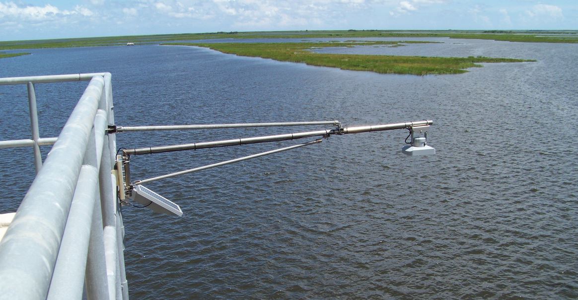 A weather sensor on a metal arm over a body of water