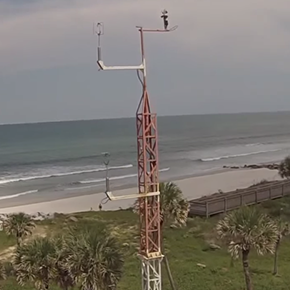 A weather antenna mounted on a large radio tower near a coastal beach
