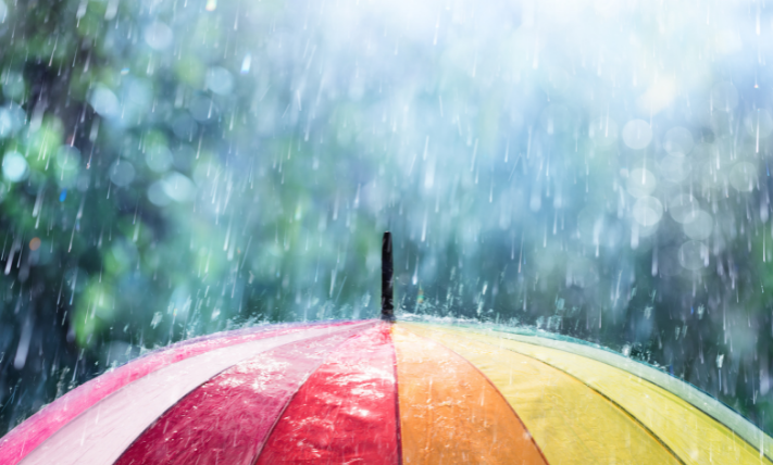 The top of a colorful umbrella being rained down on with precipitation from a storm
